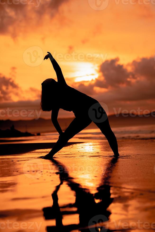 an Asian woman in silhouette is doing gymnastic movements very agile on the beach sand photo