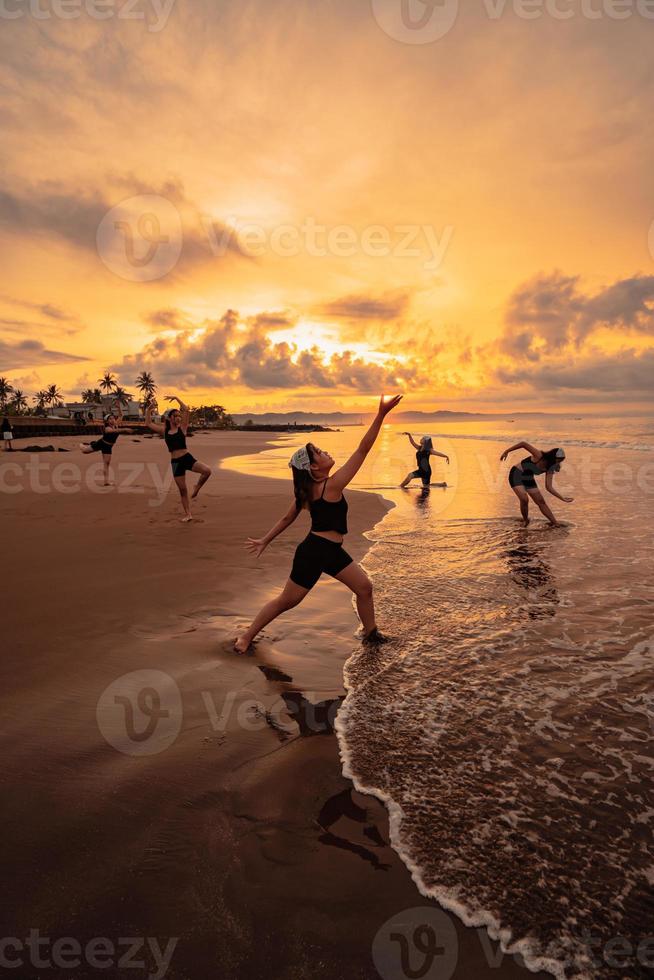 a group of Asian women is standing on the beach in black clothes and doing ballet moves in unison photo