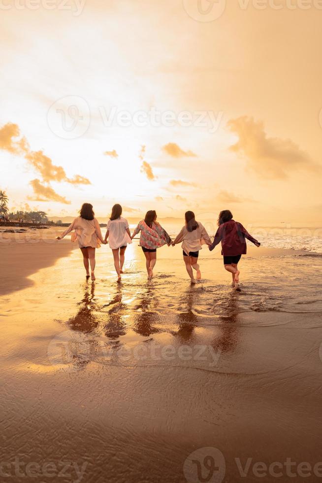 un grupo de asiático mujer es corriendo con su amigos felizmente en el playa foto