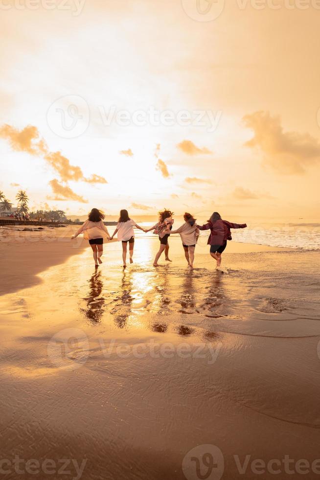 a group of Asian women is running with their friends happily on the beach photo