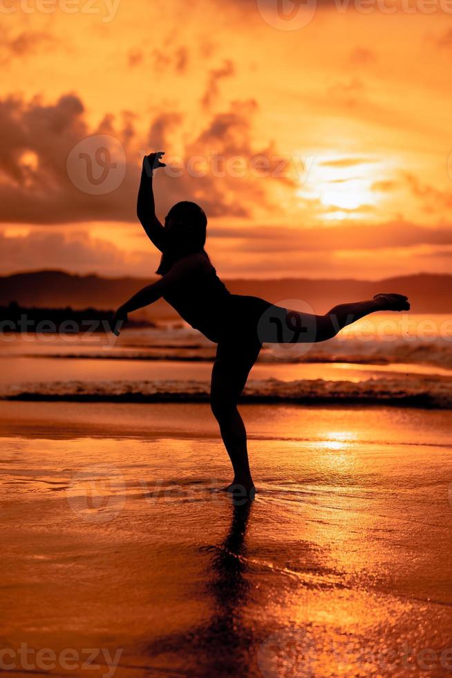 silhouette of an Asian woman dancing ballet with great flexibility and a view of the waves behind her photo