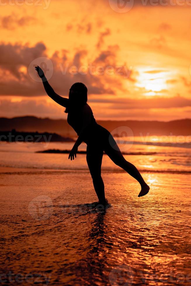 silhouette of an Asian woman dancing ballet with great flexibility and a view of the waves behind her photo