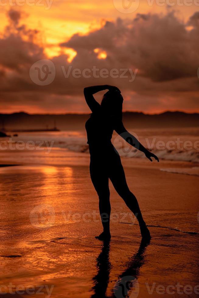 silhouette of an Asian woman dancing ballet with great flexibility and a view of the waves behind her photo