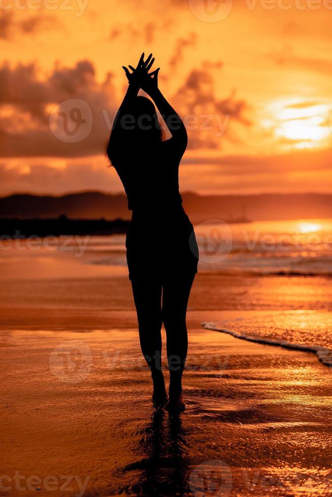 the silhouette of an Asian teenager with a tall body is dancing ballet on the waves on the beach photo