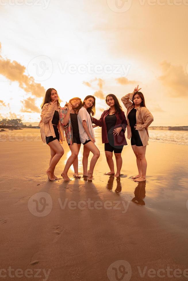 un grupo de asiático mujer en camisas posando felizmente mientras visitando un hermosa playa foto