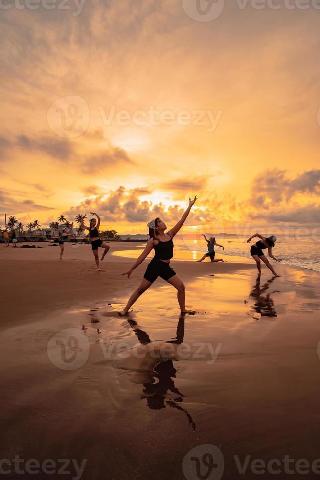 a group of Asian women is standing on the beach in black clothes and doing ballet moves in unison photo