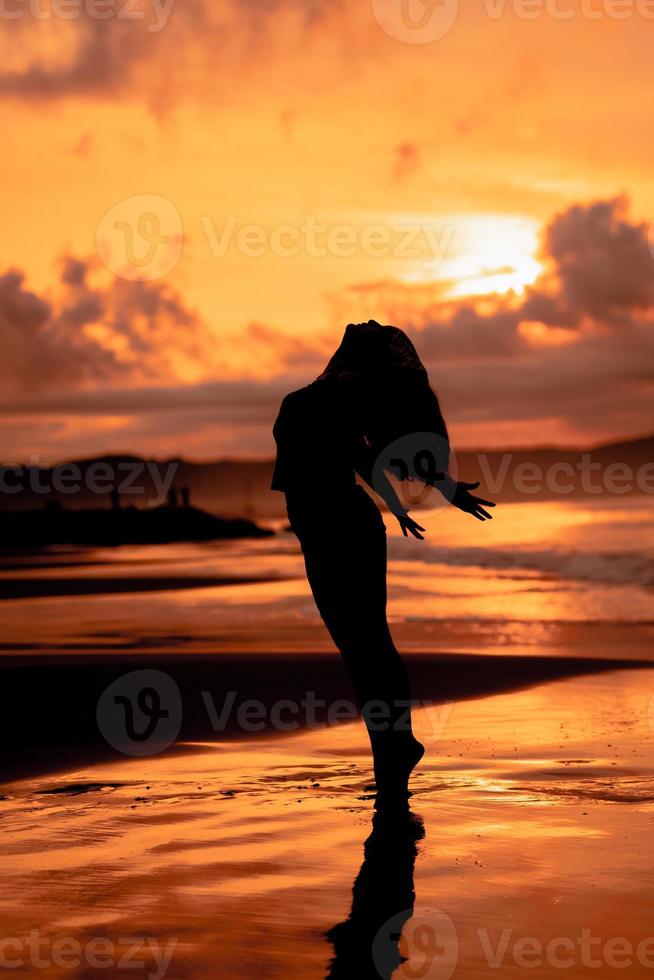 an Asian woman in silhouette is doing a very beautiful dance on the beach with the waves crashing photo