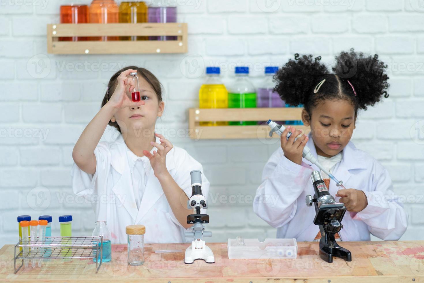 Two little kids in lab coat learning chemistry in school laboratory