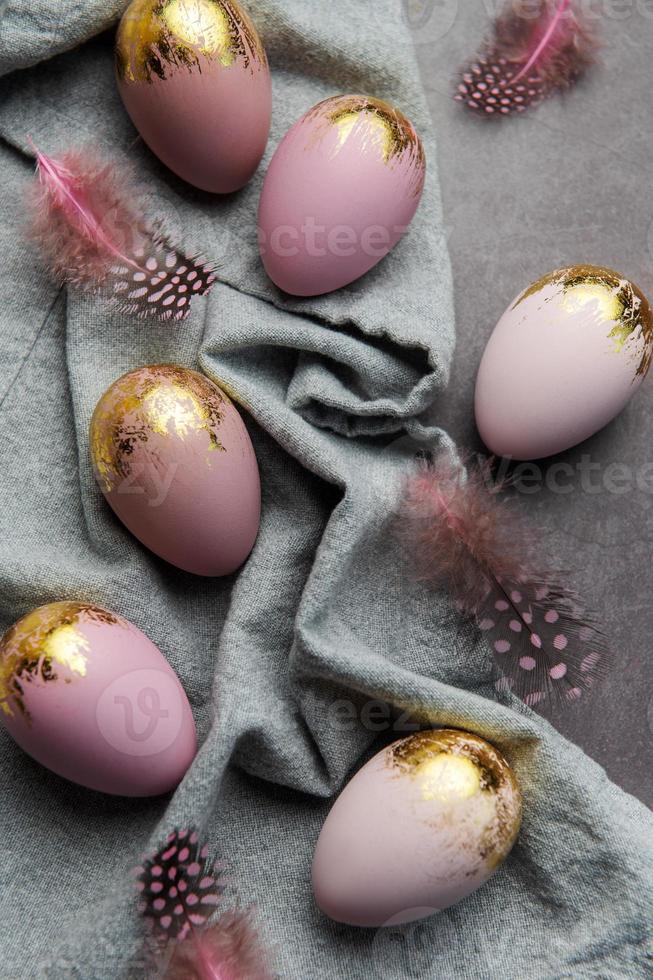los huevos de pascua están pintados con pintura violeta y dorada sobre un fondo de lino gris. foto