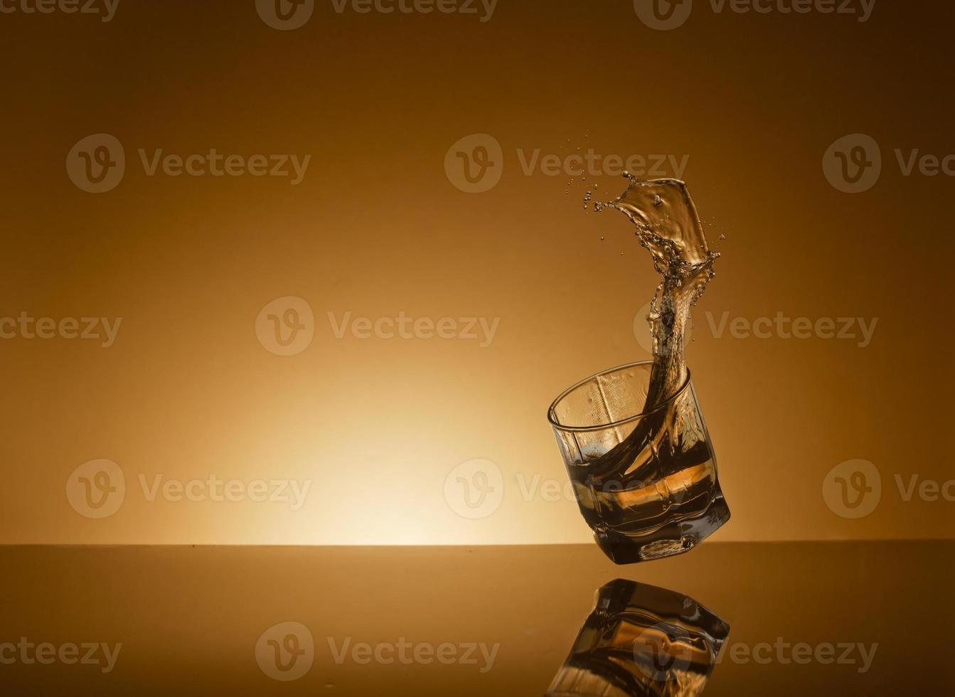 que cae vaso de alcohólico bebida en un dorado antecedentes foto