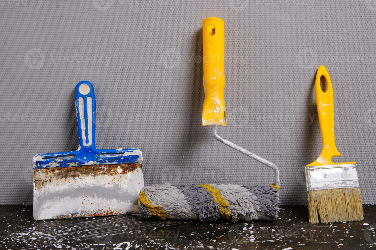 pintar rodillo, cepillo y espátula en un gris pared fondo, reparar herramienta. foto
