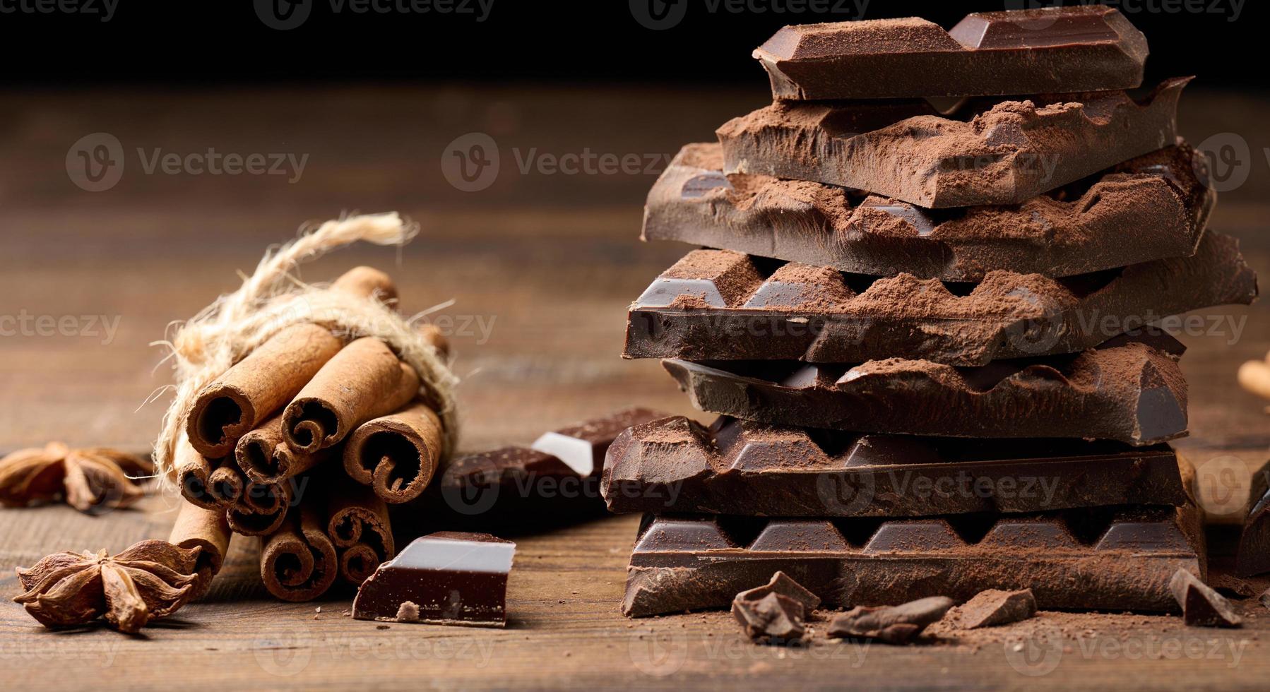 trozos rotos de chocolate negro, palitos de canela y anís estrellado sobre una mesa de madera marrón foto