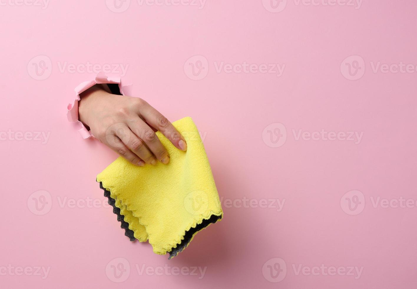 female hand sticking out of a torn hole in a pink paper background and holding a dry rag photo