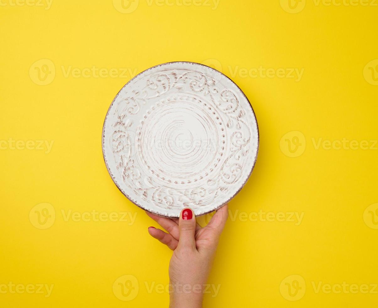 female hand holding an empty round plate on a yellow background, top view photo