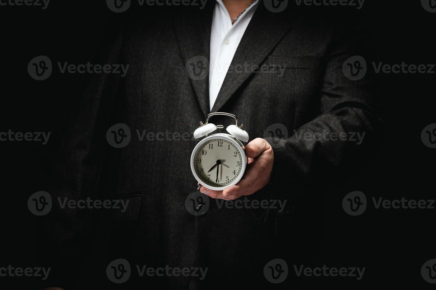 businessman in a suit holding a round alarm clock, half past seven in the morning. Clock change, early rise photo