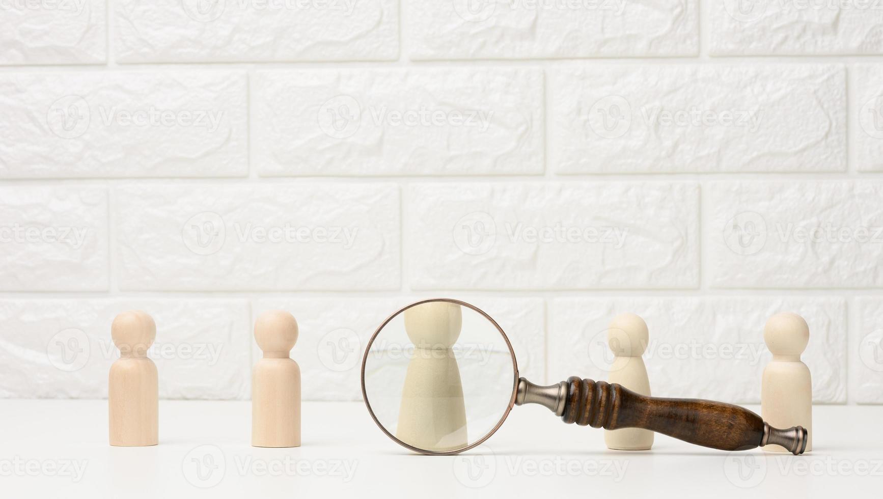 wooden figures of men stand on a white background and a magnifying glass. Recruitment concept, search for talented and capable employees, career growth photo
