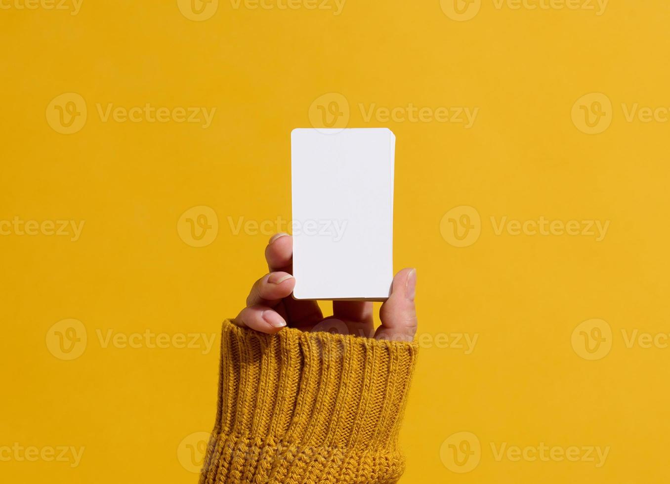 Female hand holding empty paper white business card on a yellow background. Copy space photo