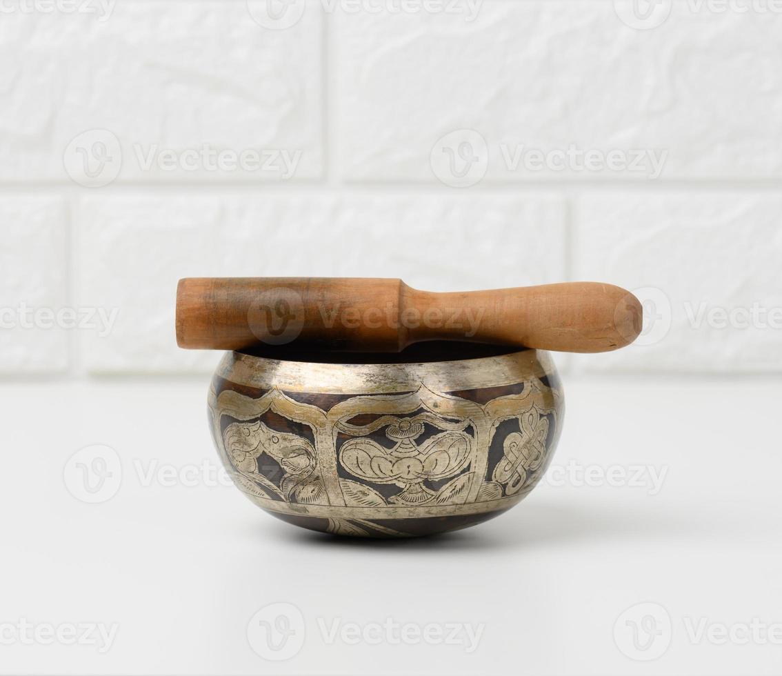 Tibetan singing copper bowl with a wooden clapper on a white wooden table, objects for meditation and alternative medicine photo