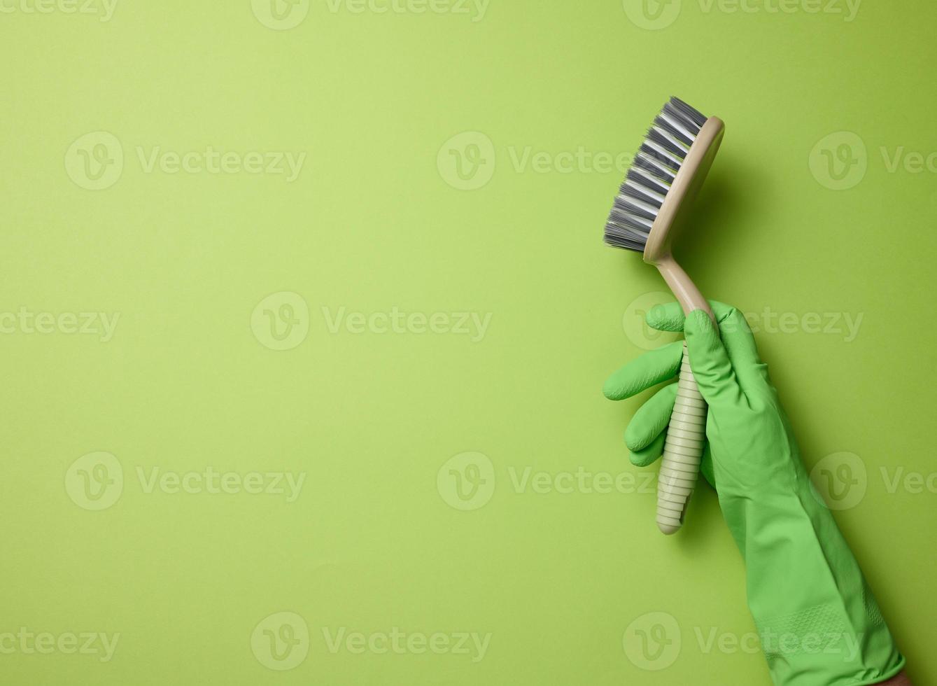 hand in a green rubber glove holds a plastic cleaning brush on a green background photo