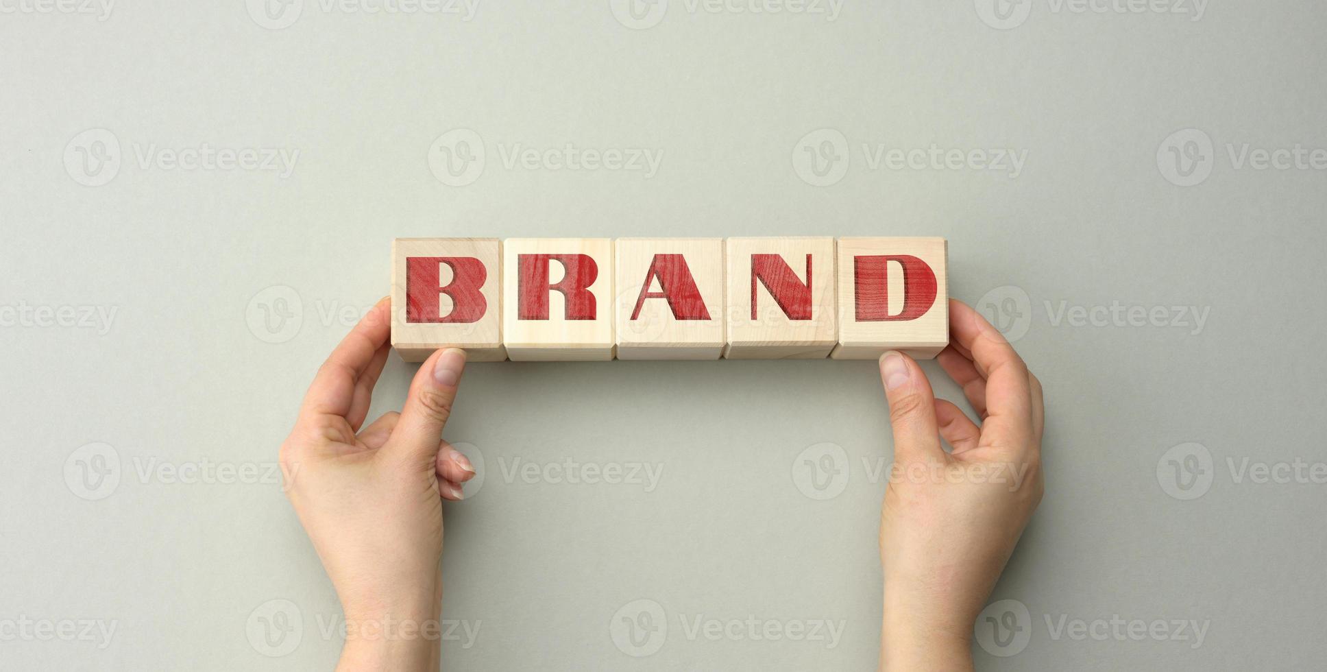 wooden blocks with the inscription brand and two female hands on a gray background. photo