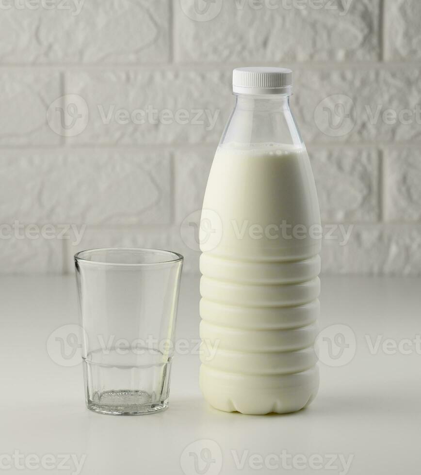 full plastic milk bottle and empty glass cup on white table, brick wall background photo