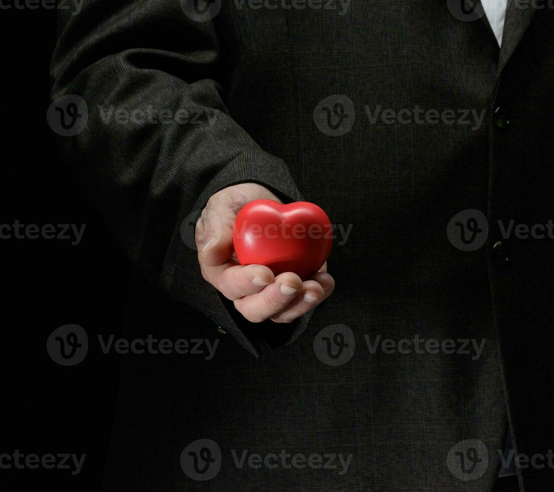 man's hand holds a red heart on a dark background photo