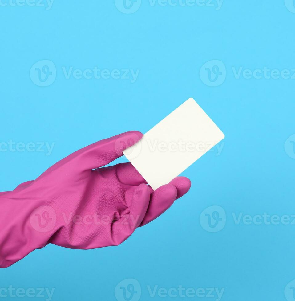 blank white cardboard business card in hand. A pink glove is on the hand, blue background photo