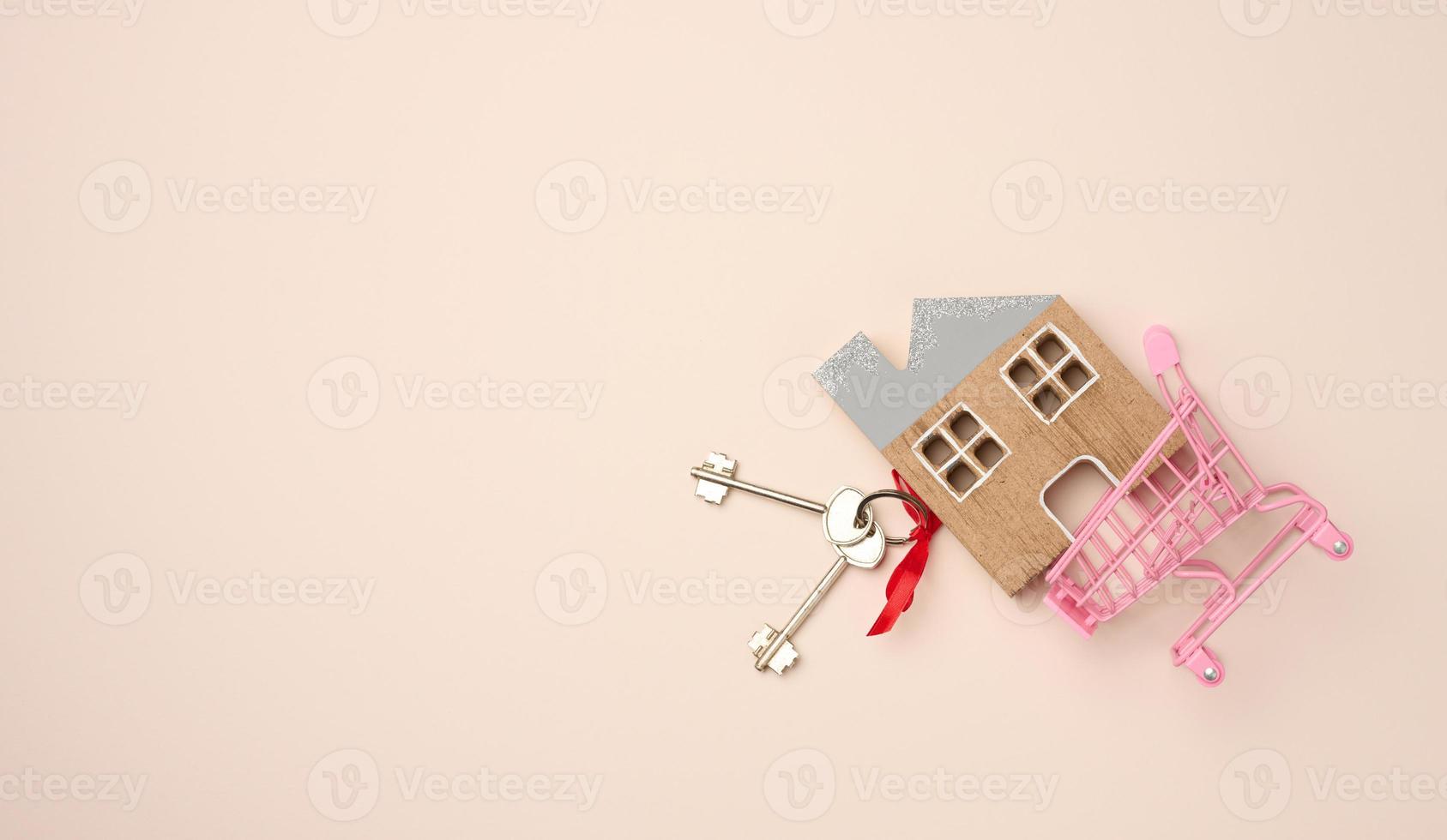 model of a wooden house, a miniature shopping cart on on a beige background. Real estate purchase photo