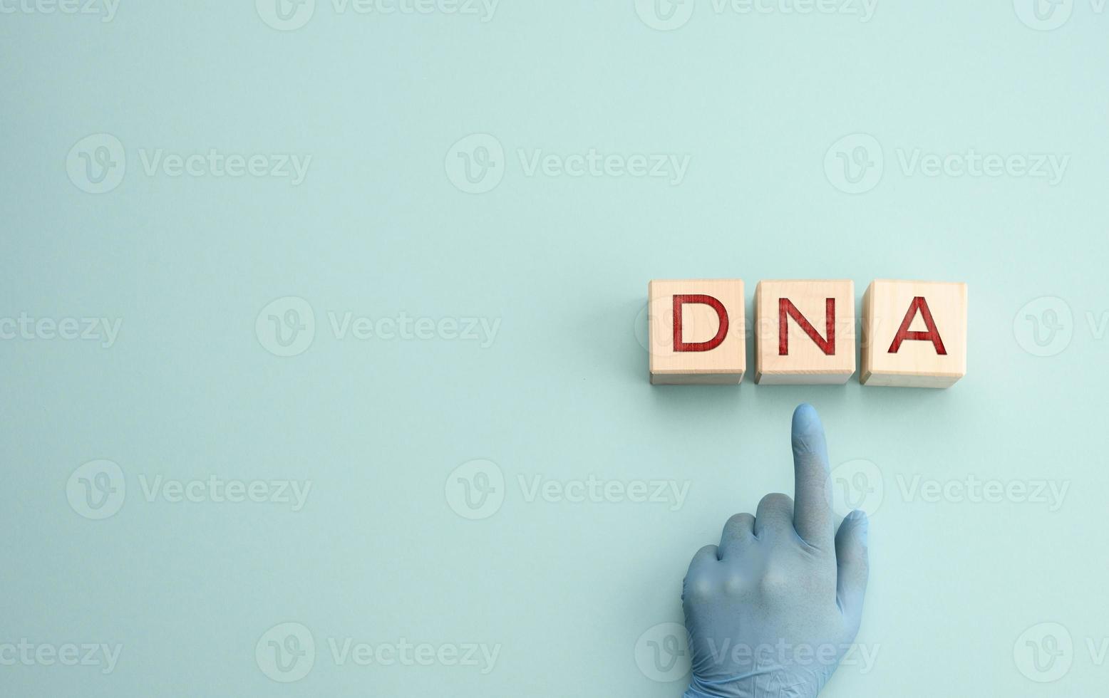 abbreviation DNA on wooden square blocks. A hand in a blue glove points to an object photo