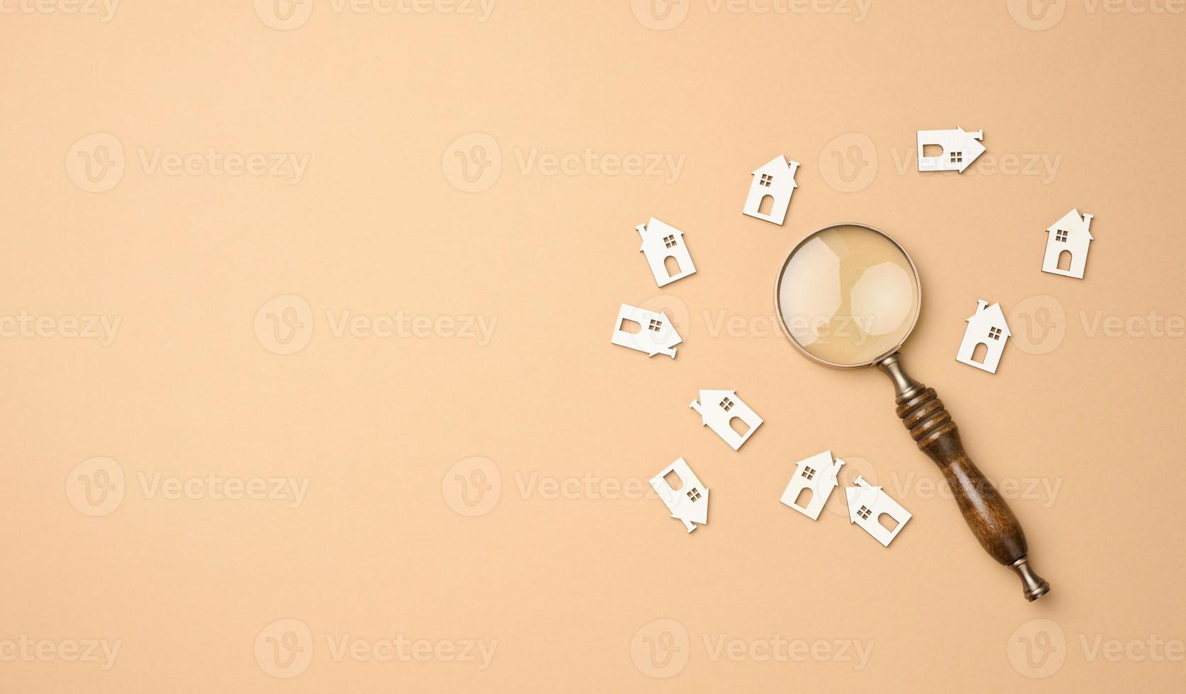 model of a wooden house and a magnifying glass on a light brown background, top view. Home search concept for rent, purchase photo