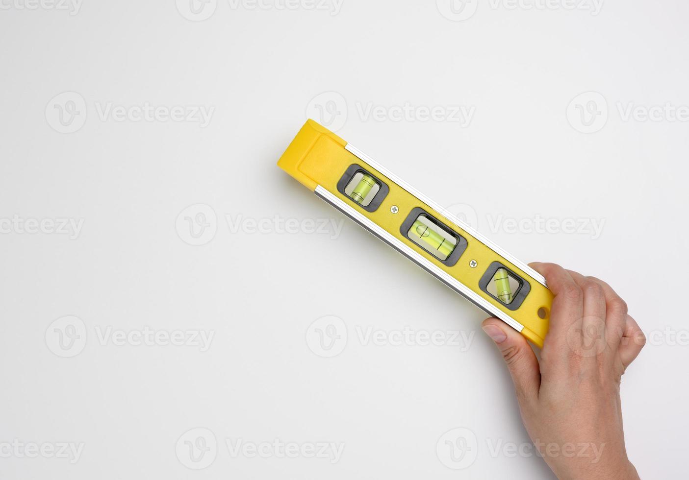female hand holds a yellow plastic building level on a white background photo