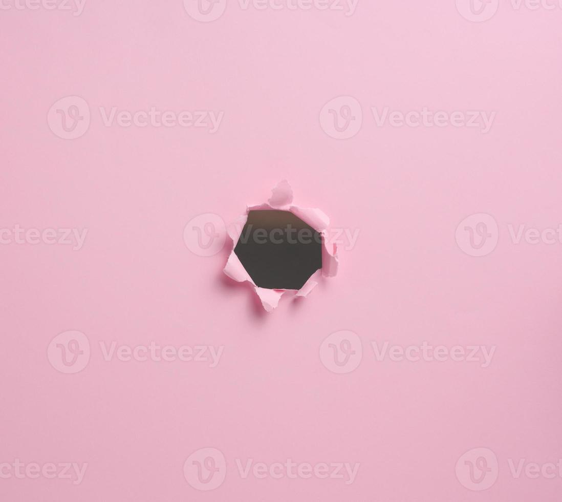 hole with torn edges in pink paper, full frame photo