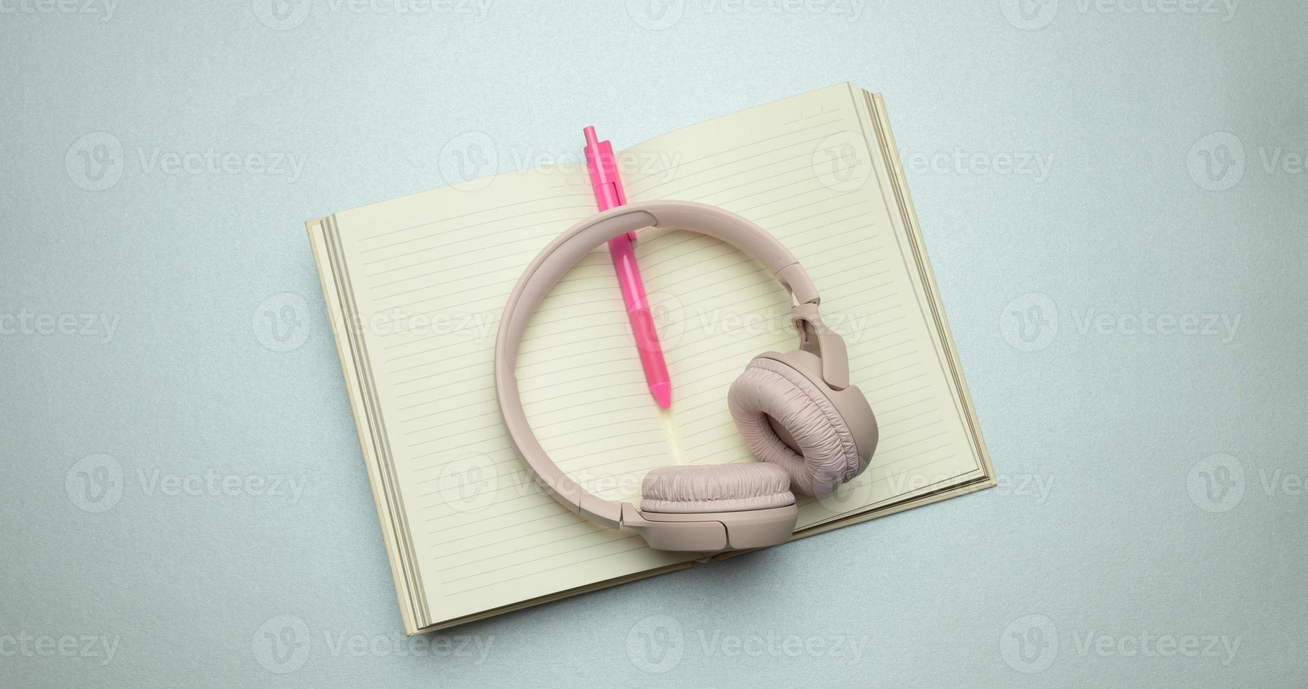 beige wireless headphones and a open notepad on a gray background photo