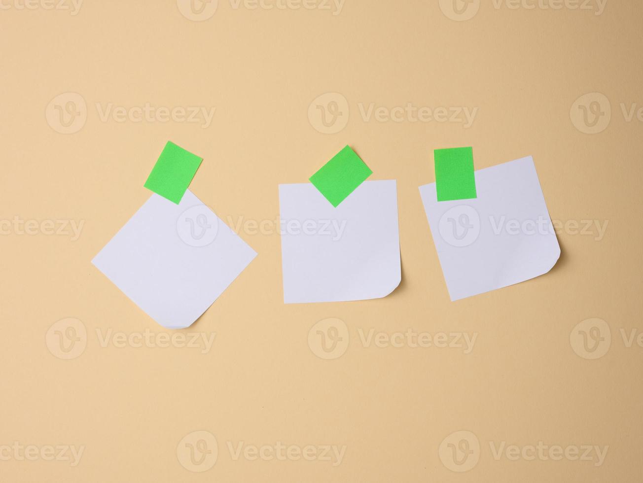 white square sheets of paper glued with green sticky paper on a light brown background photo