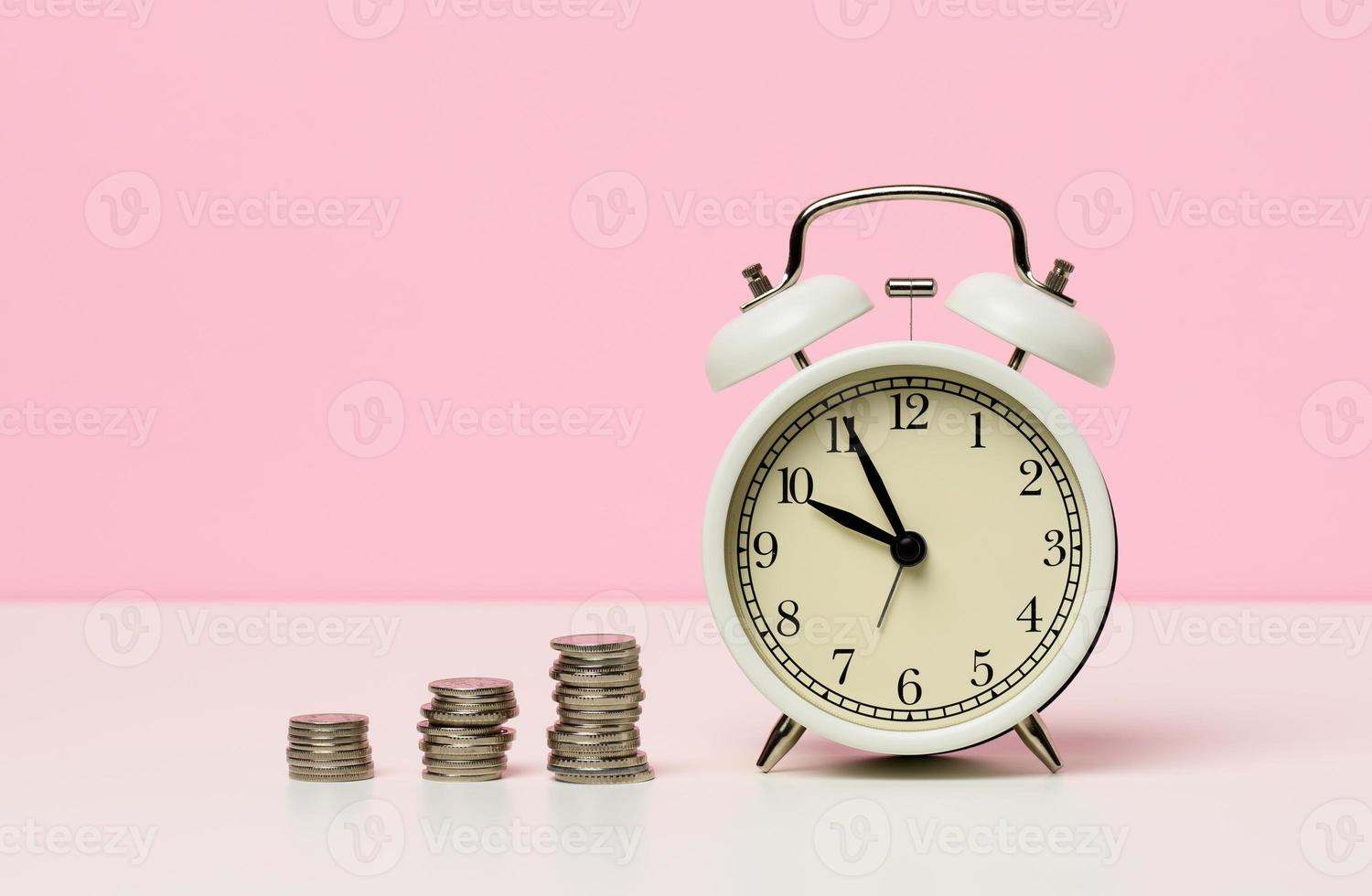 stack of coins round white alarm clock on the table. The concept of time is money, a period of discounts. photo
