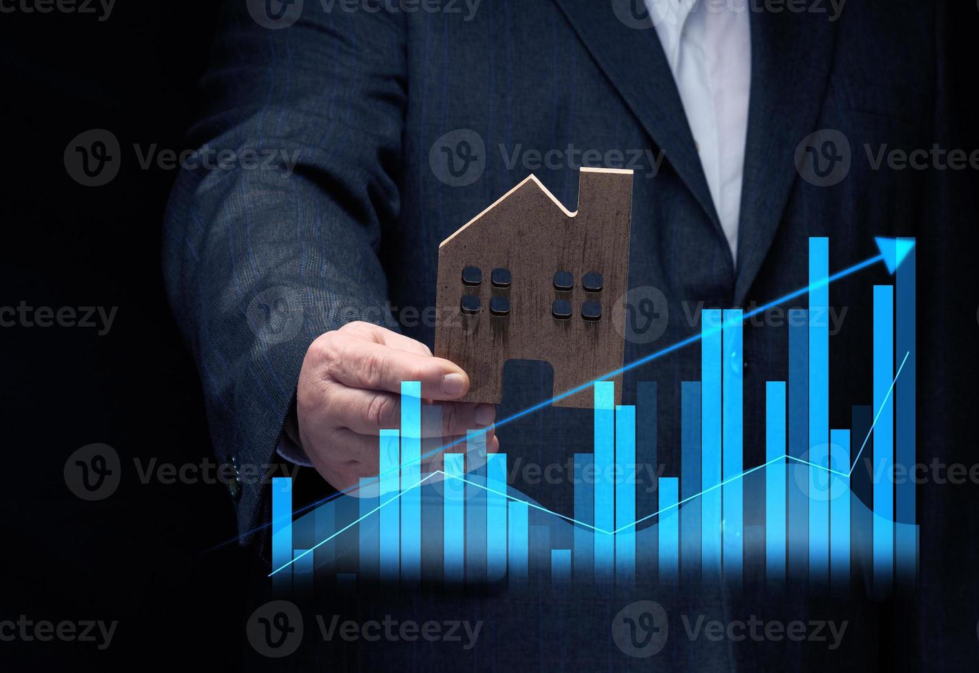 hand holds a wooden model of a house on a dark background. Real estate sale and purchase concept, rise in property prices photo