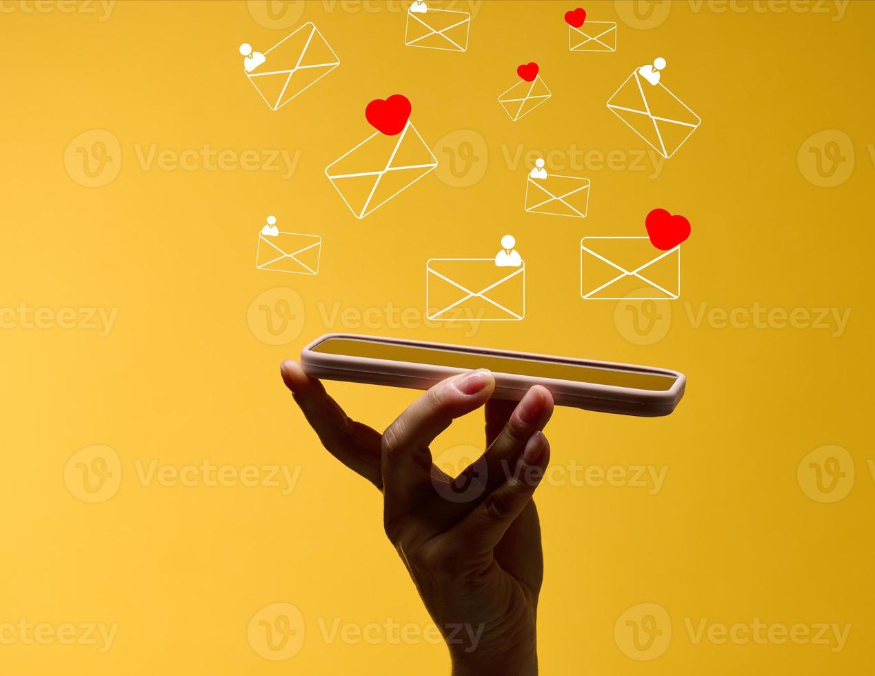 female hand holds a smartphone with flying out letters on a yellow background. Social media addiction, receiving correspondence and appraisal. photo