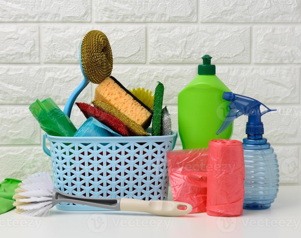 plastic basket with brushes, disinfectant in a bottle, rubber gloves on the background of a white brick wall photo