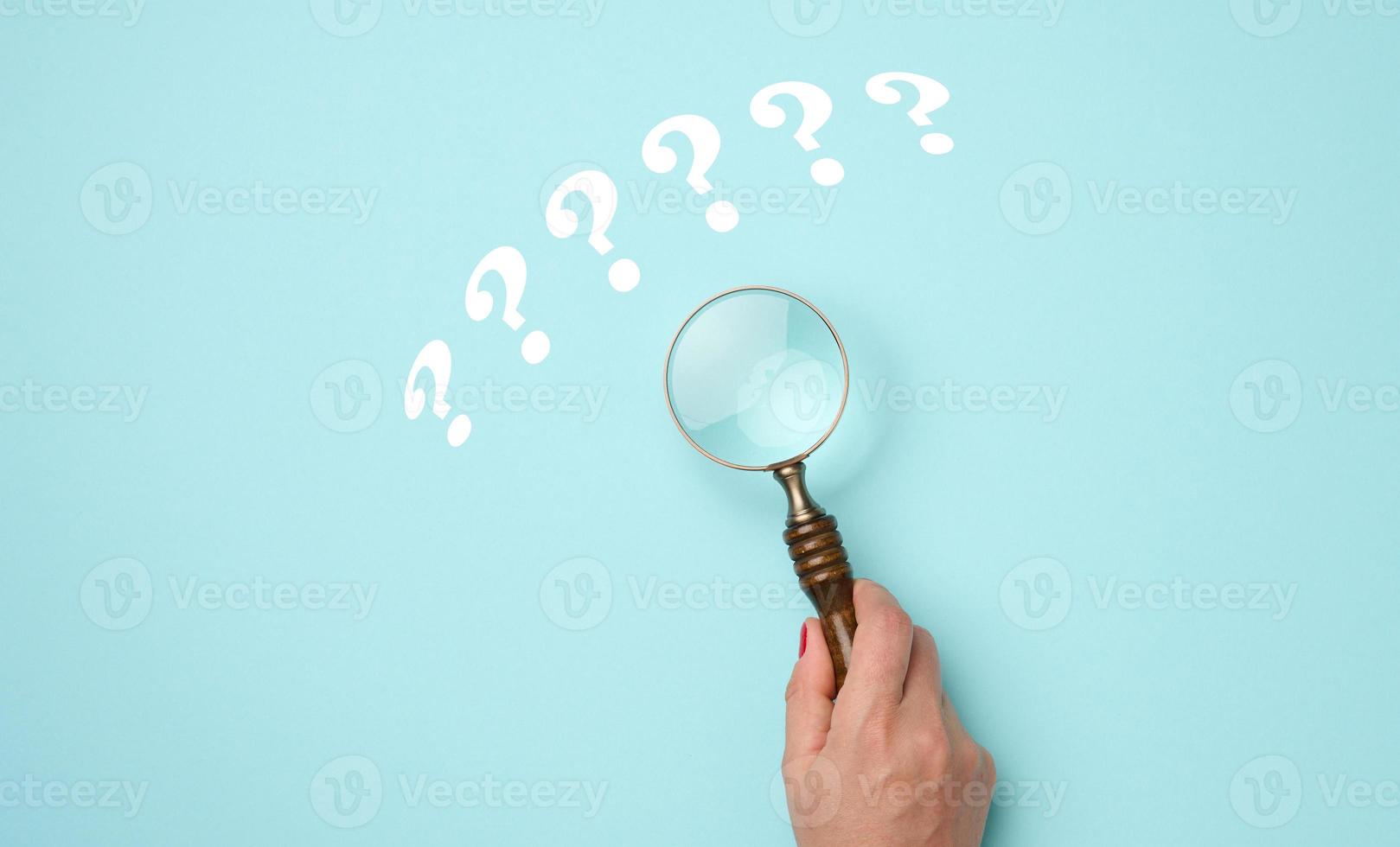 female hand holds a plastic magnifying glass and question marks on a blue background. The concept of finding an answer to questions, truth and uncertainty. photo