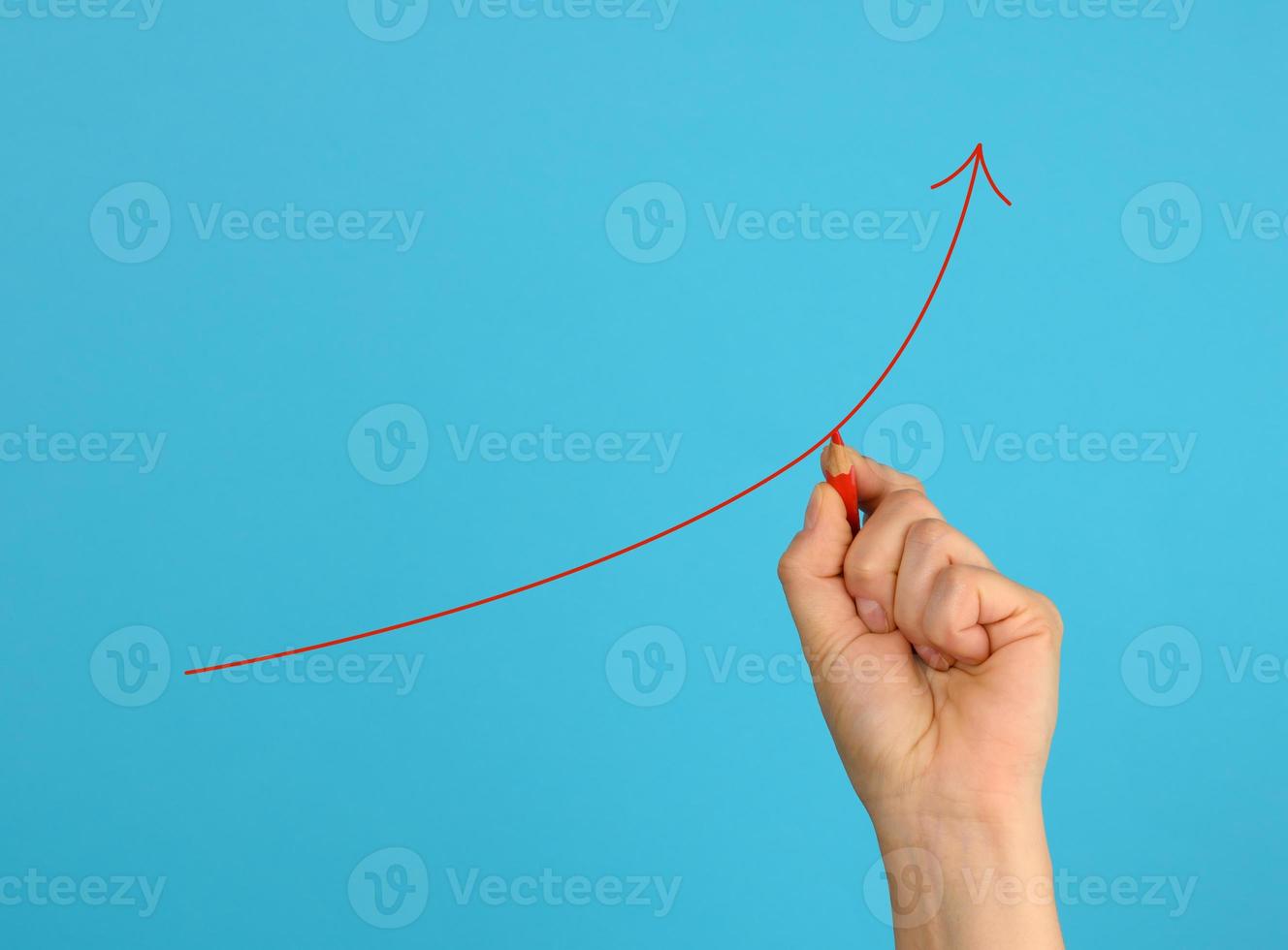 female hand draws a red up arrow on a blue background. The concept of increasing profits photo