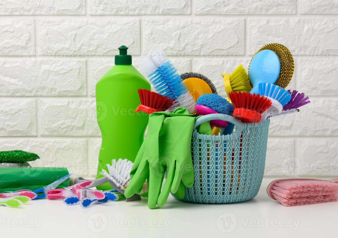 blue plastic basket with brushes, disinfectant in a bottle, rubber gloves on the background of a white brick wall photo