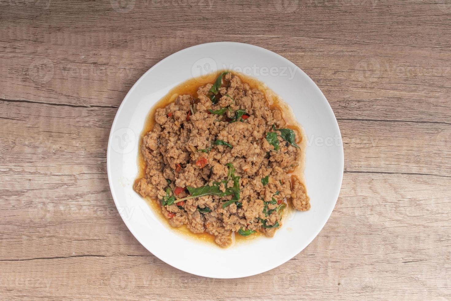 pad kaprao, pollo picado en plato blanco sobre fondo de madera foto