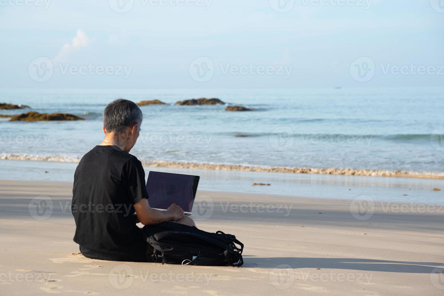 un mayor adulto utilizando computadora en el playa foto