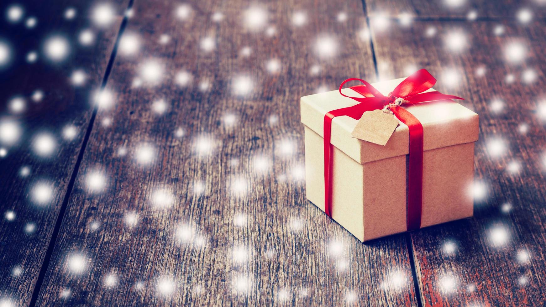 Brown gift box and red ribbon, tag with snow on wood background with space. photo