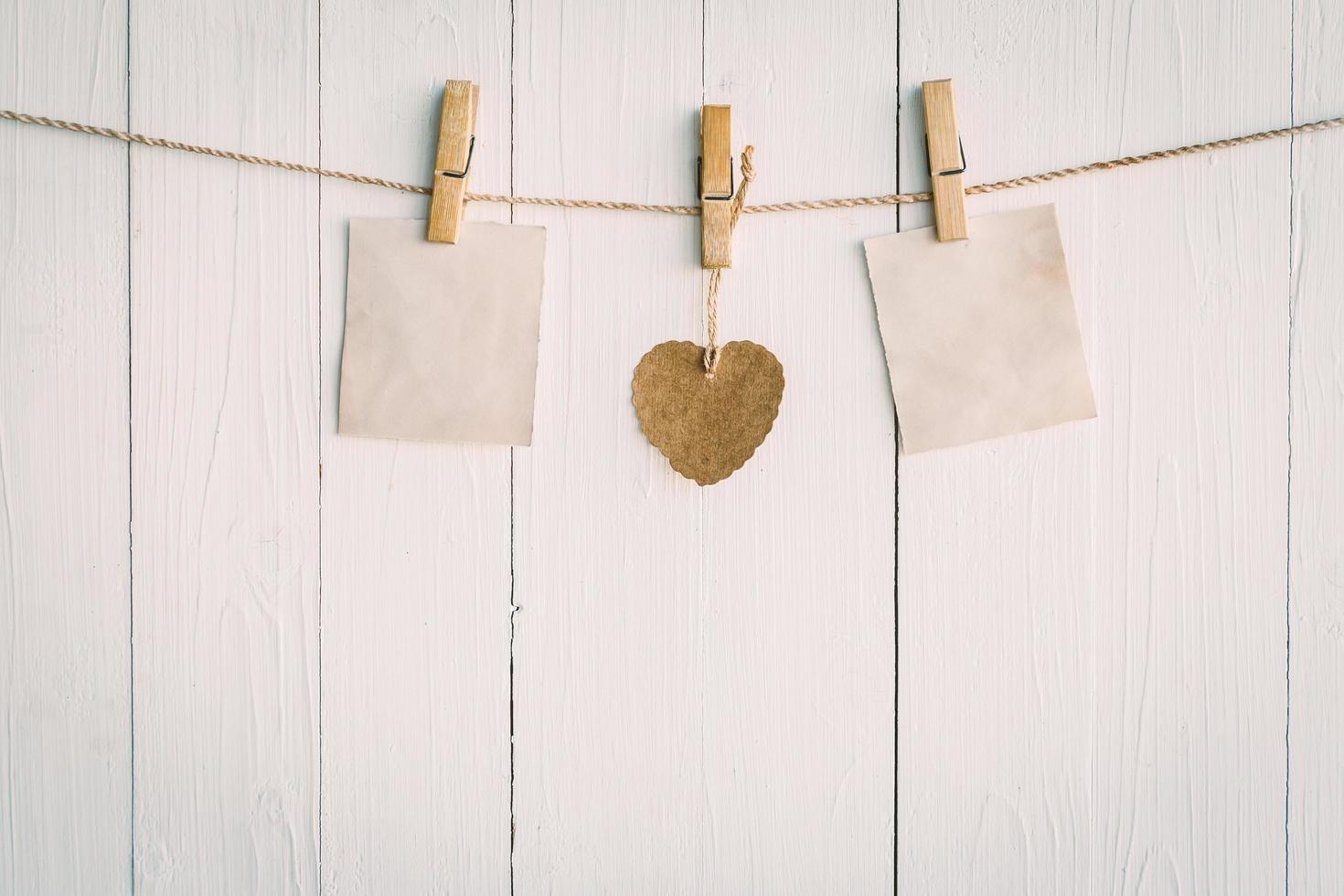 Two blank old paper and brown heart hanging. On white wooden background with vintage style. photo