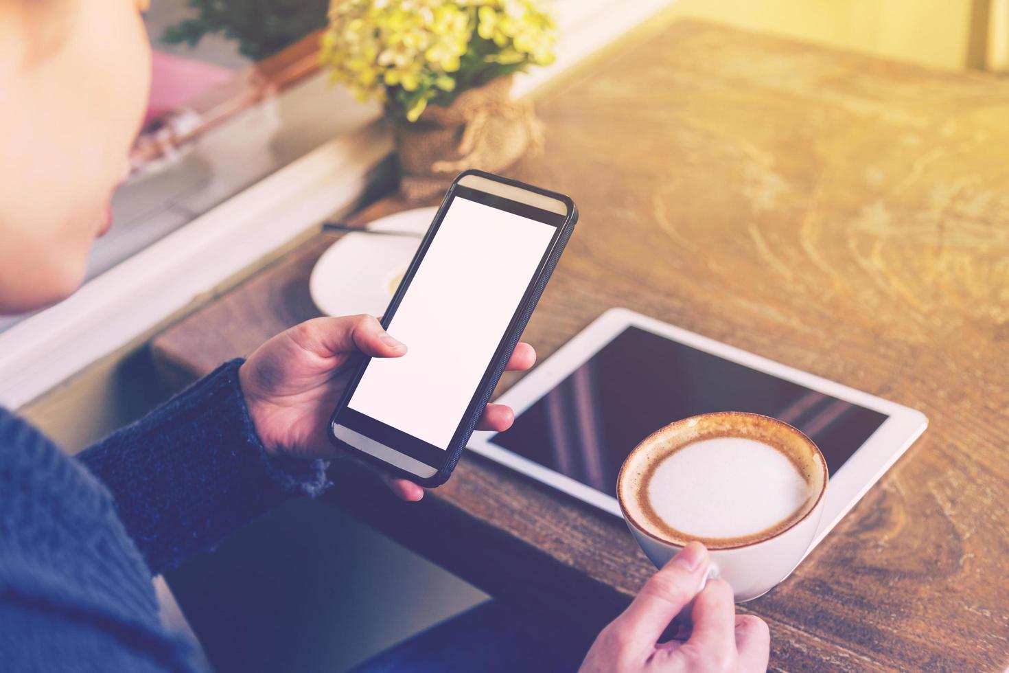 mujer jugar teléfono inteligente y bebida café con Clásico tono. foto