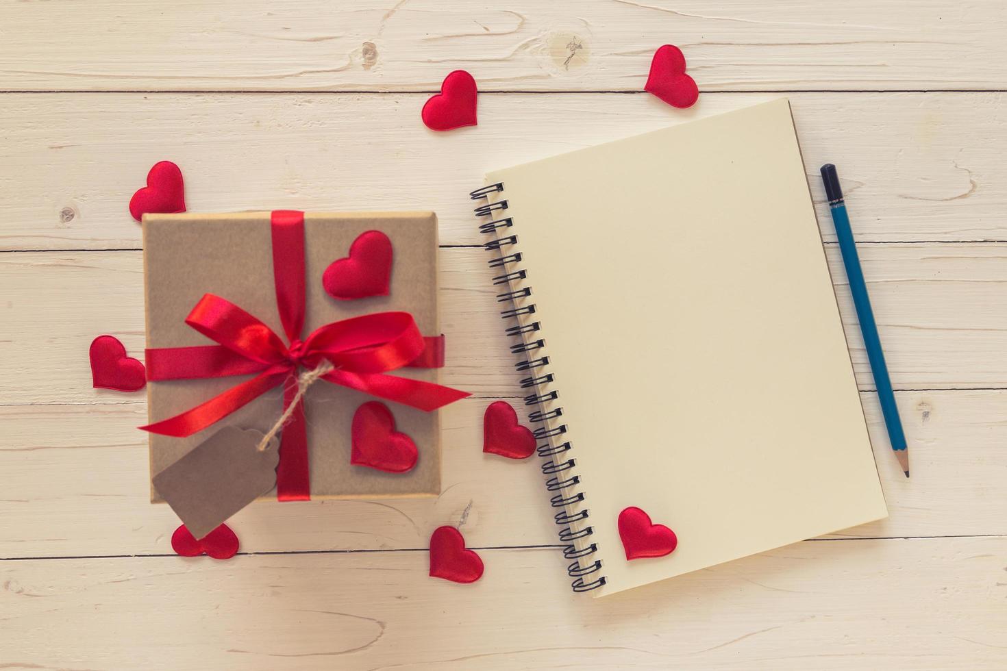 Top view gift box and red ribbon and red heart with notebook for valentine on table wooden. Valentine background. photo