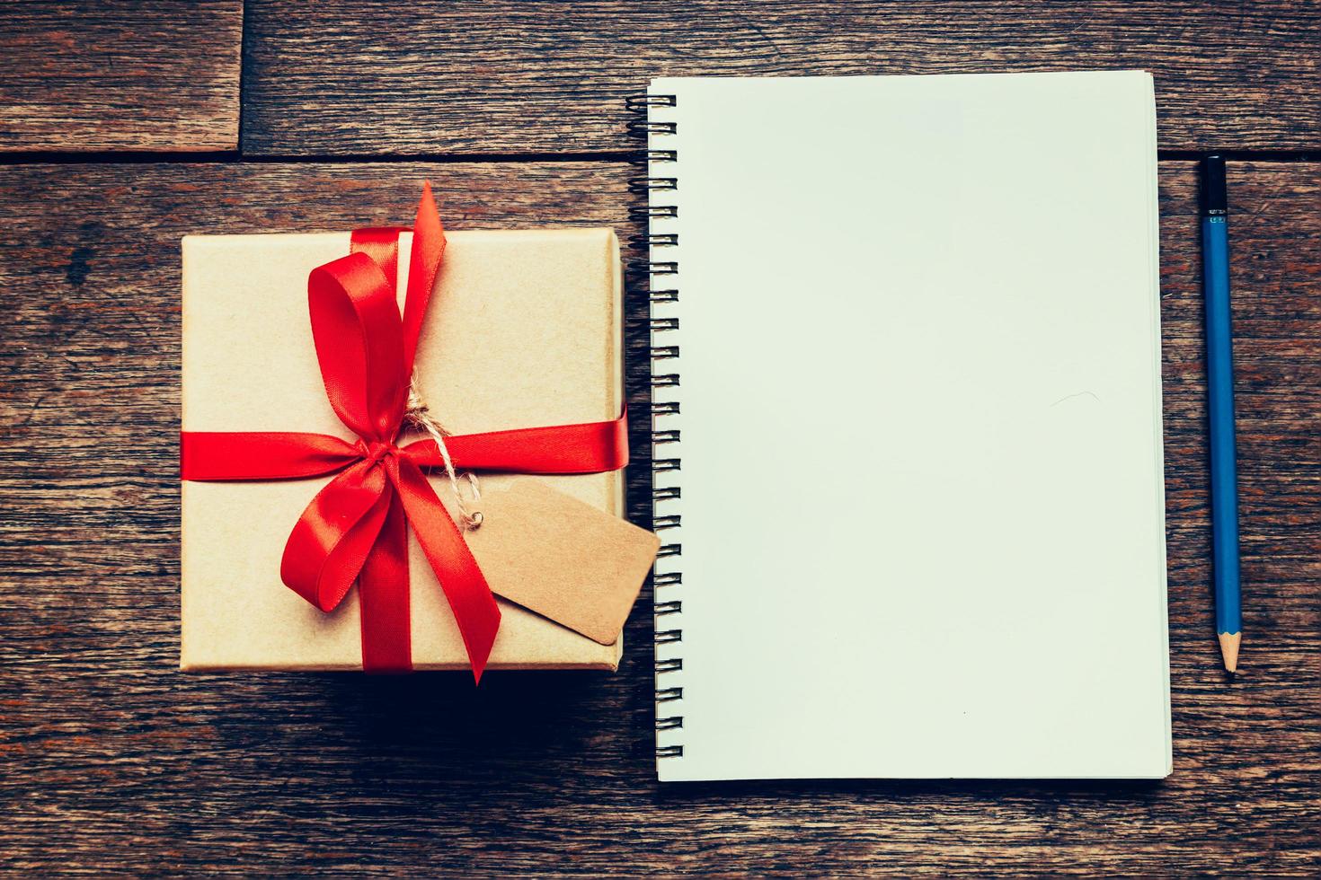 View above brown gift box and notebook with tag on wood background with space. photo