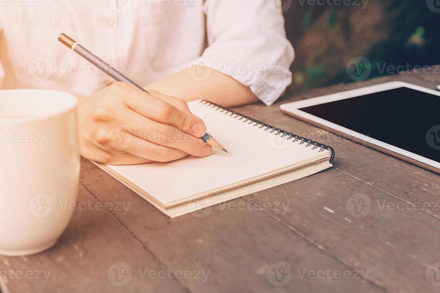 close up hand woman writing notebook in coffee shop with vintage toned. photo