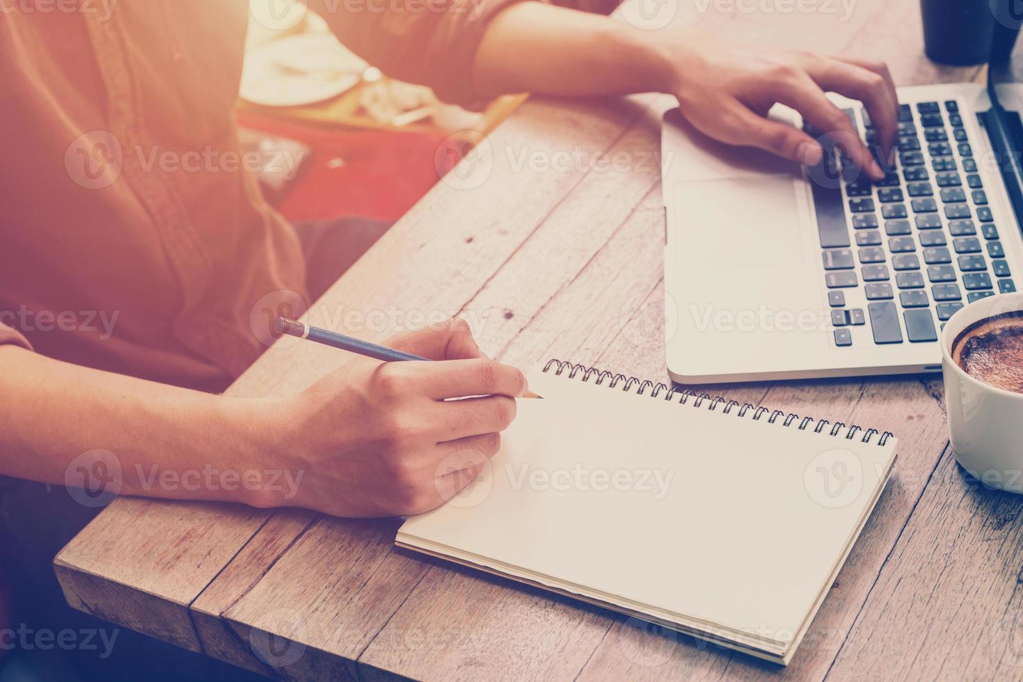 Young business man hand writing and using laptop in coffee shop with vintage filter. photo